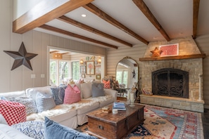 A cozy living room with a stone fireplace, a wooden ceiling, and a large star decoration. - Private River Access & Walk to Village! (Carmel Valley)
