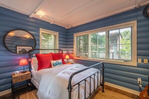 A bedroom with a bed, bedside lamps, a mirror, and a window with blinds. - Private River Access & Walk to Village! (Carmel Valley)