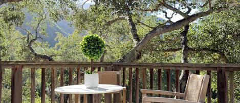 Un patio exterior con una mesa y sillas, un paraguas a rayas y vistas a árboles y montañas.