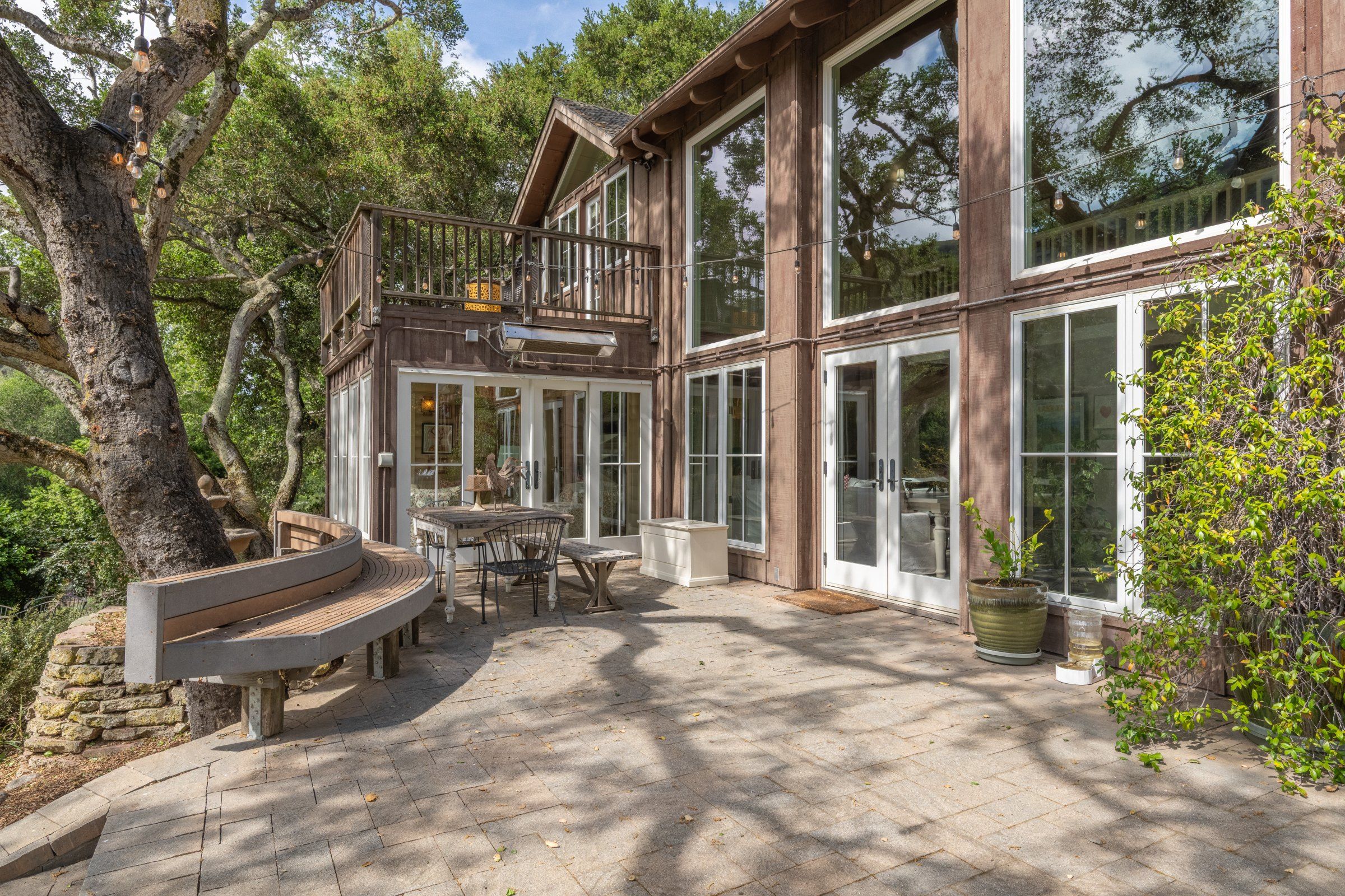 Una casa de madera con balcón, ventanas amplias y un banco de piedra.