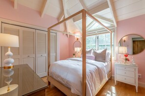 A bedroom with a four-poster bed, a bedside table with a lamp, a dresser, and a large mirror. - Private River Access & Walk to Village! (Carmel Valley)