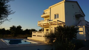 A modern two-story house with a swimming pool, a balcony, and a clear sky.