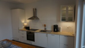 A modern kitchen with white cabinets, a stainless steel range hood, a double sink, and a built-in oven.