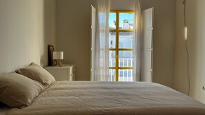 A bedroom with a bed, a bedside table with a lamp, and a window with curtains. - Villa Alhelí del Aljarafe (Mairena del Aljarafe)