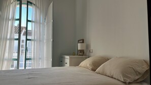 Ein Schlafzimmer mit einem Bett, einem Nachttisch, einer Lampe und einem Fenster mit Vorhängen.