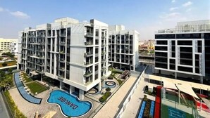 A modern multi-story building with balconies, a swimming pool, and a tennis court. - Vogue | Olivz Residence by Danube Near Dragon Mart (Dubai)