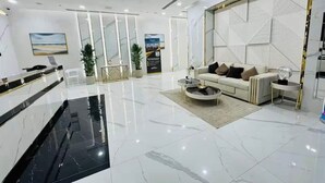 A modern hotel lobby with a marble floor, a reception desk, a seating area with a sofa and armchairs, and a decorative wall panel. - Vogue | Olivz Residence by Danube Near Dragon Mart (Dubai)