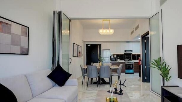 A modern living room with a sofa, coffee table, and dining area. - Vogue | Olivz Residence by Danube Near Dragon Mart (Dubai)