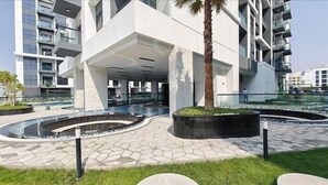 A modern building with a central atrium, a landscaped courtyard with a water feature, and a palm tree. - Vogue | Olivz Residence by Danube Near Dragon Mart (Dubai)