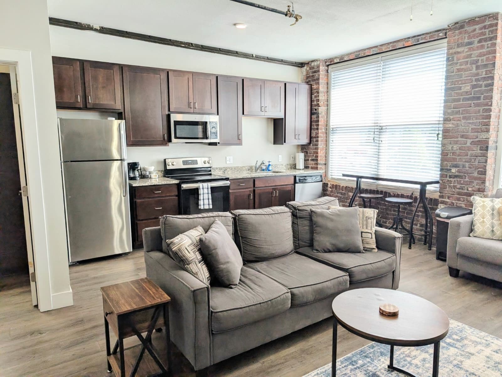 A modern kitchen with dark wooden cabinets, stainless steel appliances, and a brick accent wall.