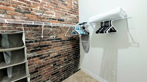 Une pièce avec un mur en briques, une armoire blanche avec des étagères et un étendoir à linge.