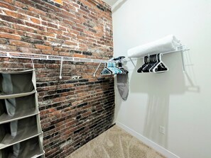 A room with a brick wall, a white closet with shelves, and a drying rack with clothes. - Popular Queen Suite w/ Parking – SLU 201 (St. Louis)
