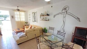 Un salon comprenant un canapé, une table à manger avec des chaises, un ventilateur de plafond et une œuvre d’art murale.