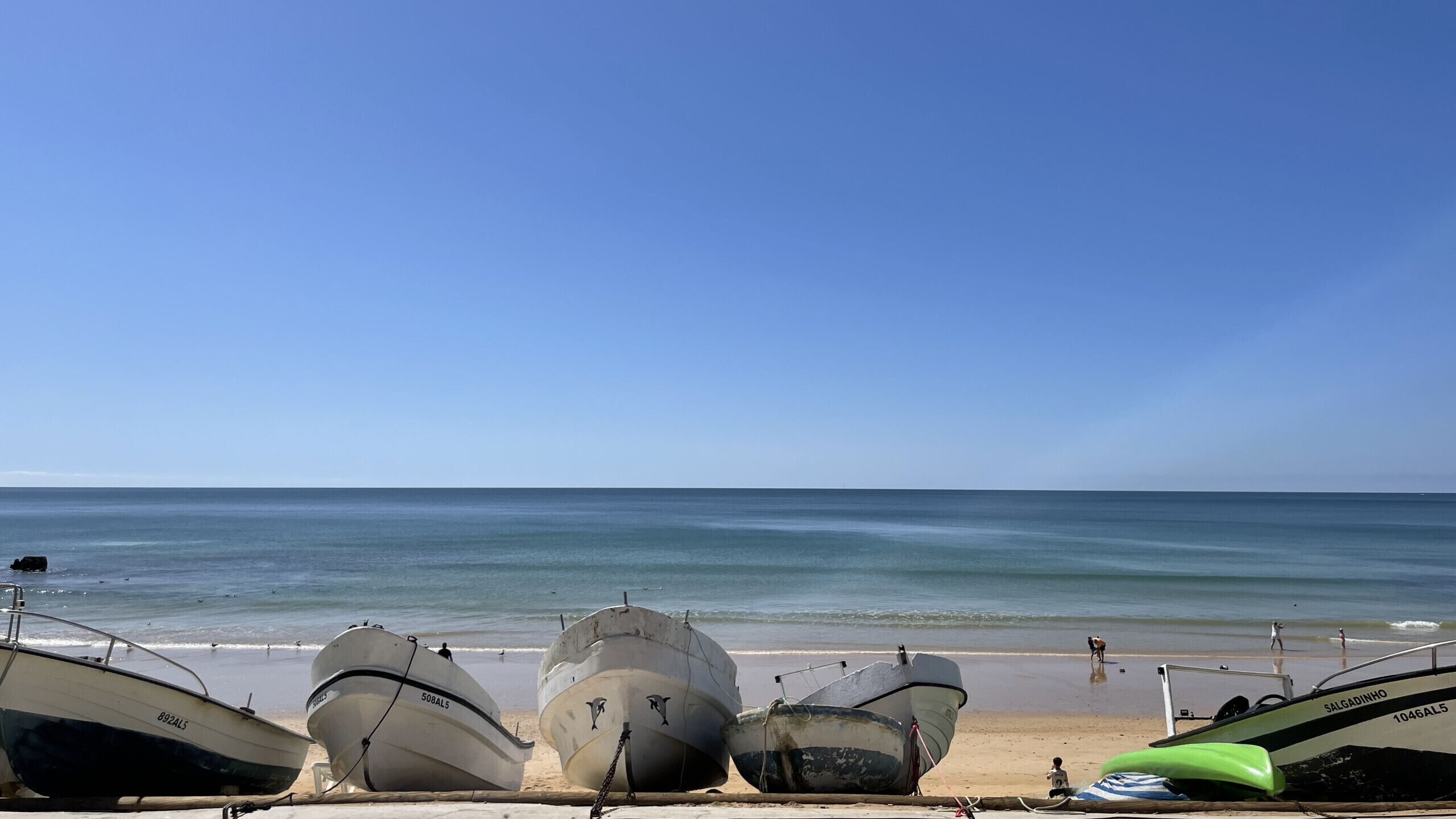 Several boats lined up on a beach with the ocean in the background.