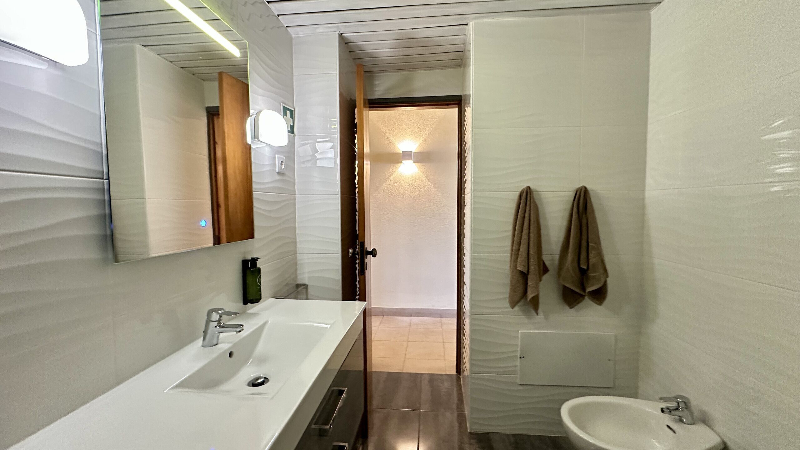 Een moderne badkamer met een grote spiegel, een wastafel, een bidet en handdoeken aan de muur.