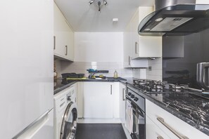 A compact kitchen with white cabinetry, a gas stove, a microwave, and a built-in oven. - Bright 2BDR Apt in Southall with Free Parking (Greater London)