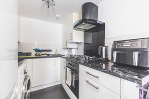 A modern kitchen with white cabinetry, a black stove, and a built-in oven. - Bright 2BDR Apt in Southall with Free Parking (Greater London)