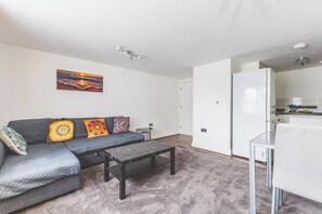 Ett modernt vardagsrum med en grå soffa, mönstrade kuddar, ett soffbord i marmor och en tavla på väggen.