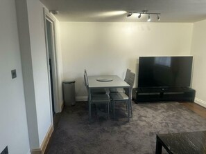 A living room with a dining table, chairs, a TV, and a trash can. - Bright 2BDR Apt in Southall with Free Parking (Greater London)