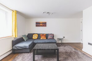 A modern living room with a grey sofa, patterned cushions, a marble coffee table, and a ceiling light fixture. - Bright 2BDR Apt in Southall with Free Parking (Greater London)