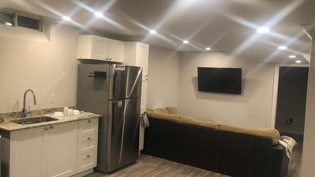 Una cocina compacta con refrigerador empotrado, un lavamanos y un televisor de pantalla plana montado en la pared.
