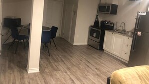 Cocina compacta con armarios blancos, microondas y refrigerador. Cuenta con una zona de comedor con mesa y sillas.