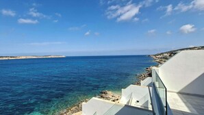 Vista sulla costa con mare blu cristallino, litorale roccioso e architettura moderna.
