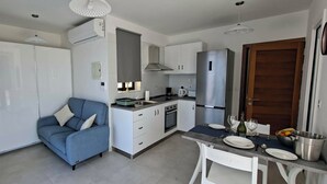 Una cucina compatta con mobili bianchi, un divano blu, un tavolo da pranzo con sedie e un frigorifero.
