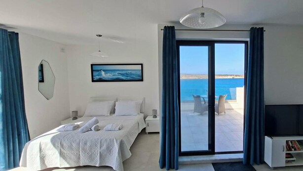 Camera d'albergo con un letto, una televisione, una libreria, un quadro e vista sul mare.