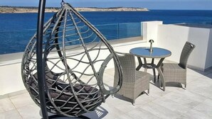 Una poltrona amaca, un tavolino rotondo e due sedie su una terrazza con vista sul mare.