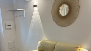 A living room with a beige sofa, a glass coffee table, a blue chair, a round mirror, and a wall-mounted light fixture. - Getaway & Wellness (Ravenel)