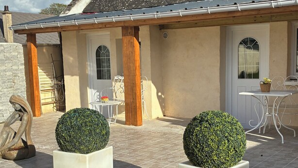 A house with a tiled roof, a white door, and a small patio area with two potted topiaries and a metal sculpture. - Getaway & Wellness (Ravenel)
