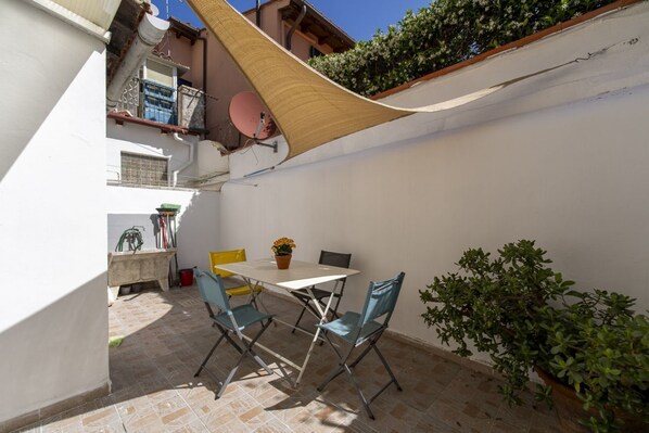 Un patio con una mesa, sillas, una pérgola colgante y una planta en maceta.