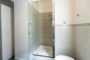 Un baño con cabina de ducha de vidrio, inodoro y paredes con azulejos.