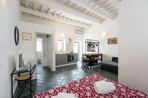 Una habitación con cama, escritorio, silla, kitchenette y baño.