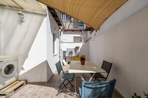 Un espacio exterior reducido con una mesa, sillas, lavadora y una planta en maceta.