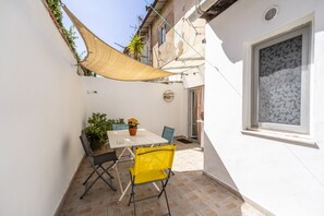 Un pequeño patio con una mesa y sillas, un toldo colgante y una ventana con diseño de hojas.