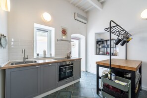 Ett modernt kök med gråa skåp, en bänkskiva i trä, en inbyggd ugn, en diskho och en hylla med kastruller och stekpannor.