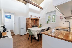 Una cocina moderna con encimera de madera, zona de comedor con sillas, refrigerador blanco y ventana con vista a zonas verdes.