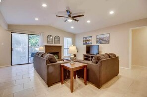 A living room with a ceiling fan, a fireplace, a TV, and a sofa. - Quiet & Spacious 3BR Austin Retreat with Patio, Workspace+ Hotel-Style Amenities (Austin)