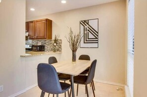 A dining area with a table and chairs, a kitchen in the background, and a framed abstract artwork on the wall. - Quiet & Spacious 3BR Austin Retreat with Patio, Workspace+ Hotel-Style Amenities (Austin)