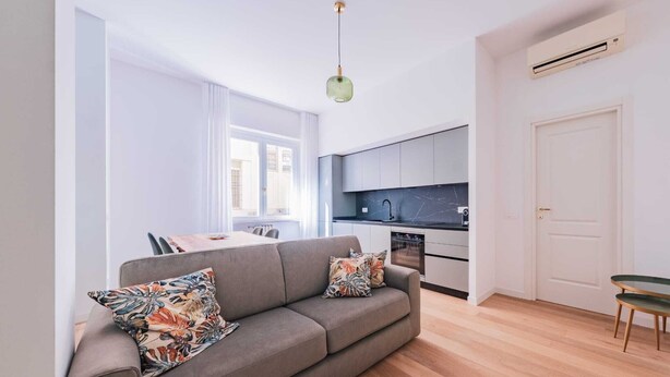 Eine moderne Wohnung mit grauem Sofa, einem Esstisch, einer Küchenzeile und Blick auf die Stadt.