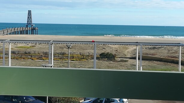Vista de la playa con un muelle, una valla y cielo despejado.