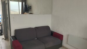 Un sofá gris con cojines rojos, un televisor sobre un mueble bajo y una ventana con cortinas.