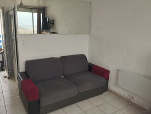 A grey sofa with red cushions, a TV on a stand, and a window with curtains. - Incredible sea view (Leucate)