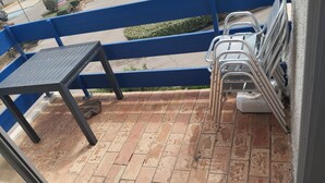 Un patio con una mesa y sillas, barandal azul y vista a la calle.