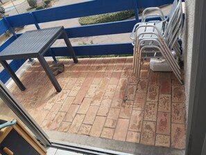 A patio with a table and chairs, a blue railing, and a view of the street. - Incredible sea view (Leucate)