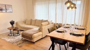 A living room with a sofa, a dining table set for four, and a small side table. - 3BR | parking, WLAN, home office, balcony, view, fully equipped. Kitchen (Bad Mergentheim)