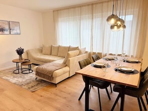 Ein Wohnzimmer mit einer Couch, einem Esstisch für vier Personen und einem kleinen Beistelltisch.