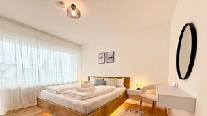 A modern bedroom with a wooden bed, bedside tables, a desk, and a large mirror. - 3BR | parking, WLAN, home office, balcony, view, fully equipped. Kitchen (Bad Mergentheim)